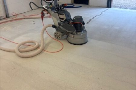Betonslijpmachine met aangesloten stofzuiger tijdens het schuren van een betonvloer
